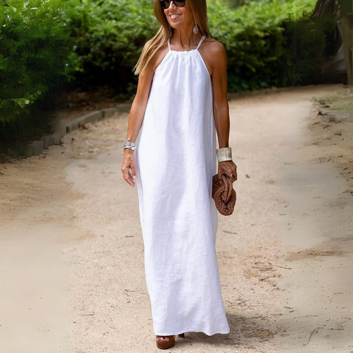 Frau in weißem Sommerkleid spaziert auf sandigem Weg, umgeben von grüner Natur. Elegantes Outfit, Sommermode, Freizeitkleidung, Damenmode.