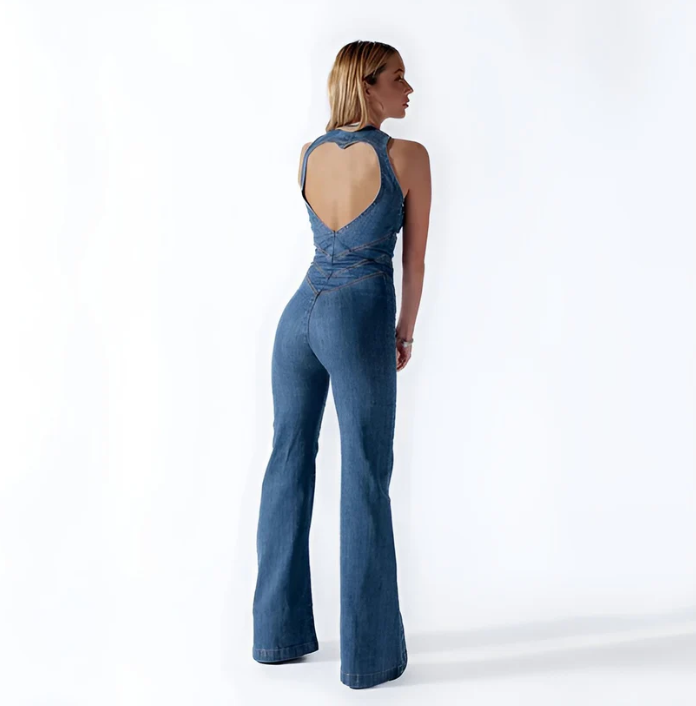 Frau in modischem, rückenfreiem Jeans-Jumpsuit mit ausgestelltem Bein, trendige Damenmode, stilvolles Outfit, Rückansicht, weißer Hintergrund.
