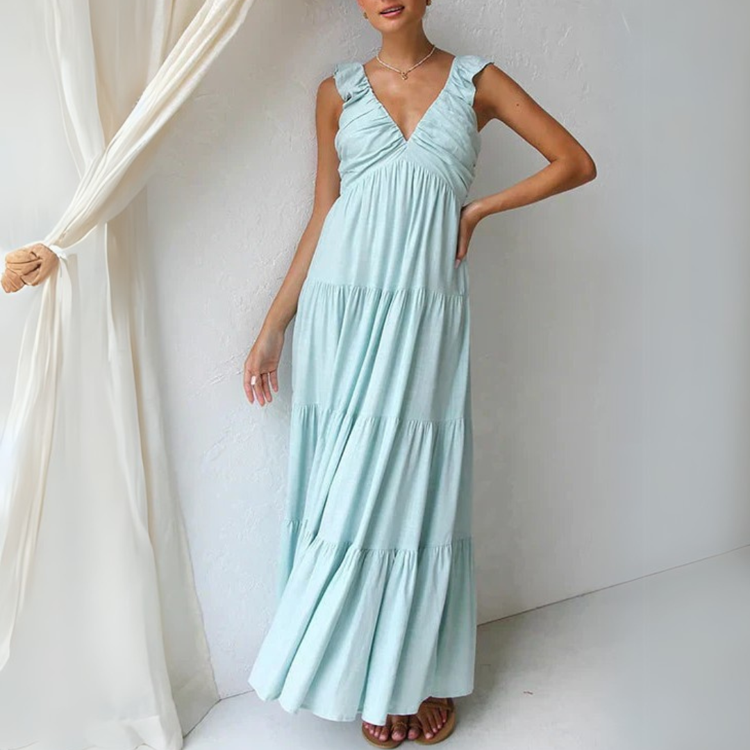 Frau in langem, hellblauem Sommerkleid mit Rüschenärmeln steht vor weißer Wand. Elegantes Maxikleid, modisches Design, luftiger Stoff.