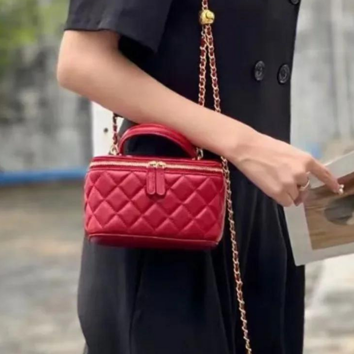 Frau mit roter, gesteppter Handtasche und goldener Kette, trägt schwarzes Kleid. Modische Damenaccessoires, elegantes Design.