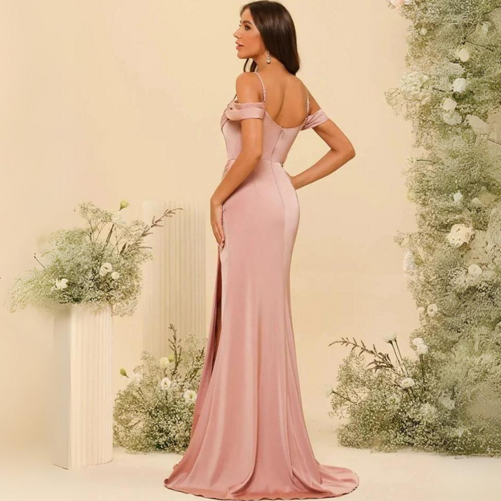 Frau in elegantem, rosa Abendkleid mit Schulterträgern, umgeben von Blumenarrangement. Perfekt für formelle Anlässe und Hochzeiten.