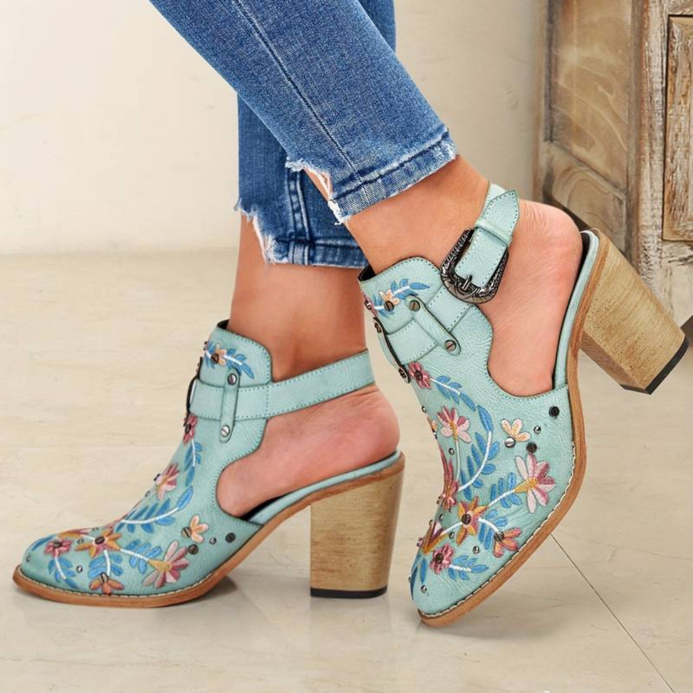 Hellblaue, bestickte Cowboystiefel mit Absatz und Blumenmuster, getragen mit zerrissenen Jeans. Modische Damenstiefel, ideal für trendige Outfits.