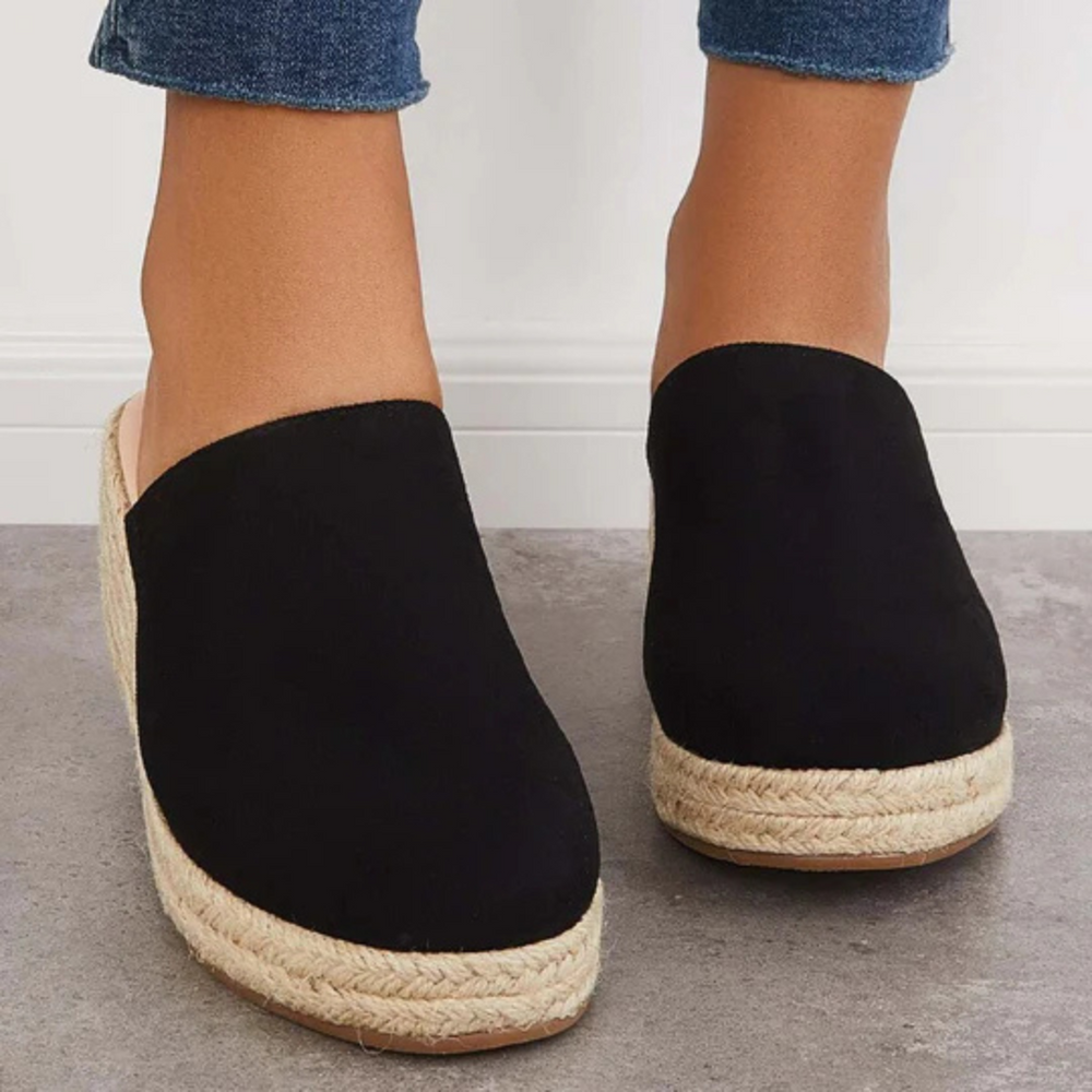 Schwarze Espadrille-Pantoletten mit geflochtener Sohle, getragen von einer Person in blauen Jeans. Bequeme Sommerschuhe für Damen.