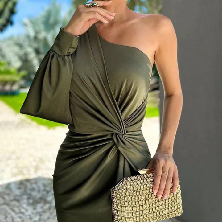 Frau in einem eleganten, einärmeligen, olivgrünen Kleid mit Knoten-Detail, hält eine goldene Clutch. Perfekt für Abendmode und stilvolle Anlässe.