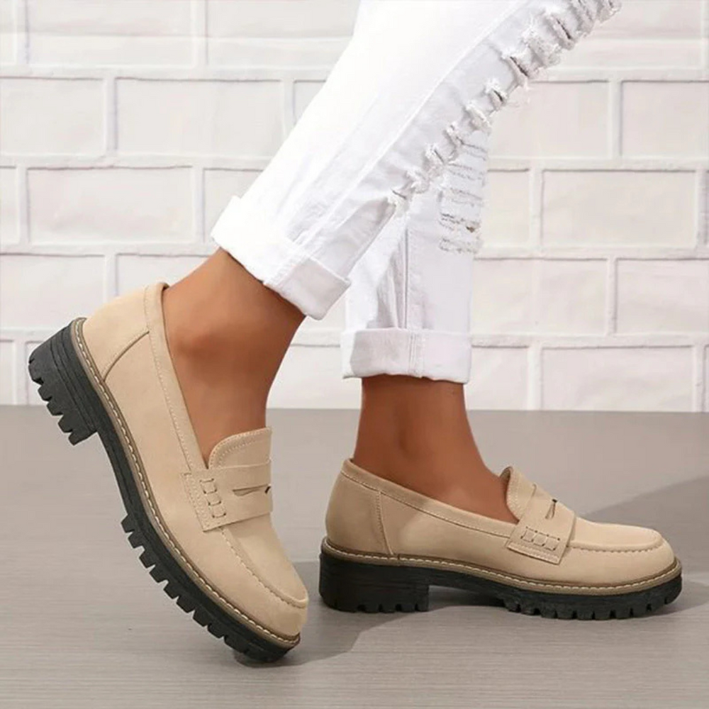 Beige Damen-Loafer mit dicker Sohle, getragen zu weißen, zerrissenen Jeans vor einer weißen Ziegelwand. Modische, bequeme Schuhe für den Alltag.