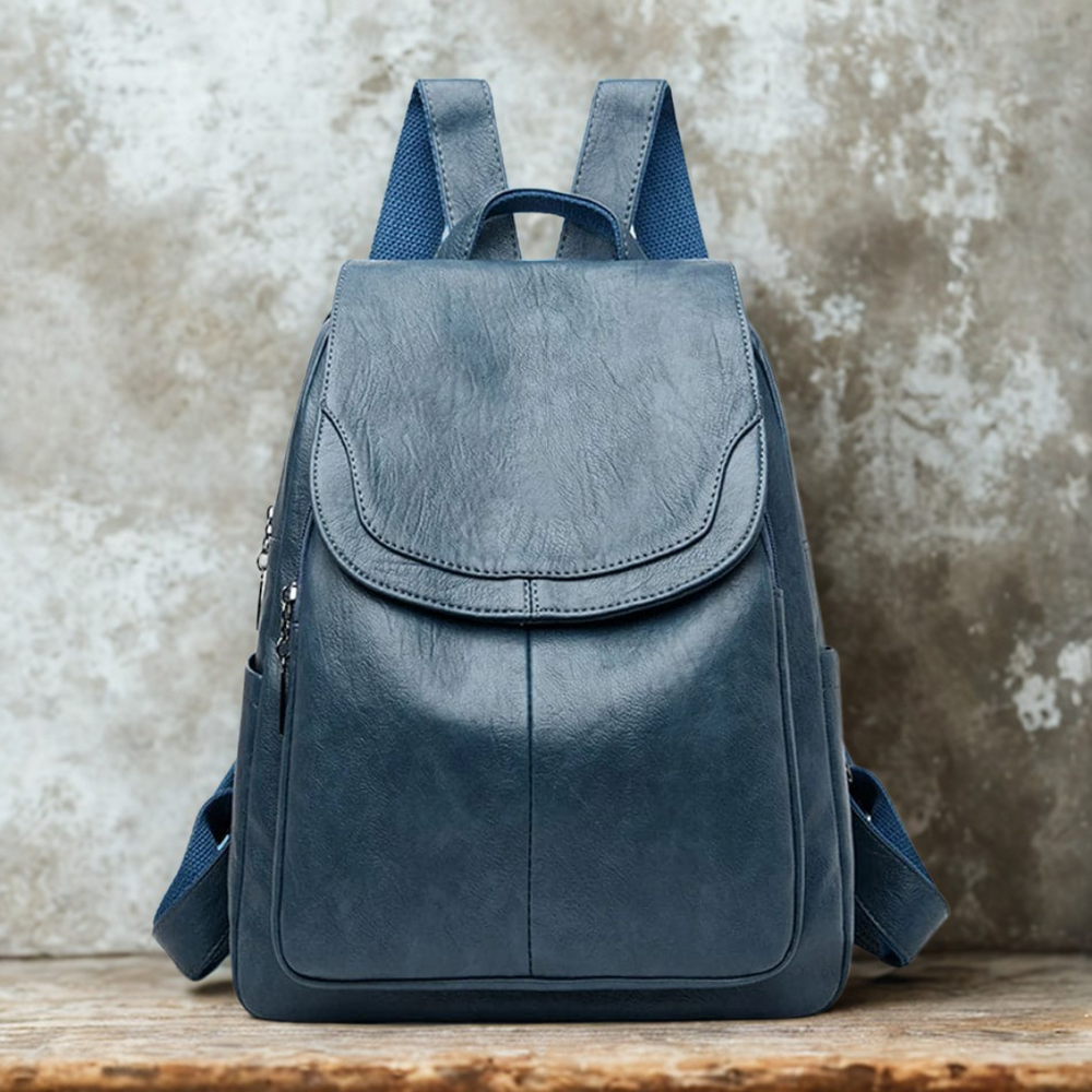 Dunkelblauer Lederrucksack auf rustikalem Holztisch vor Betonwand. Moderner, stilvoller Rucksack für Damen, ideal für Alltag und Reisen.