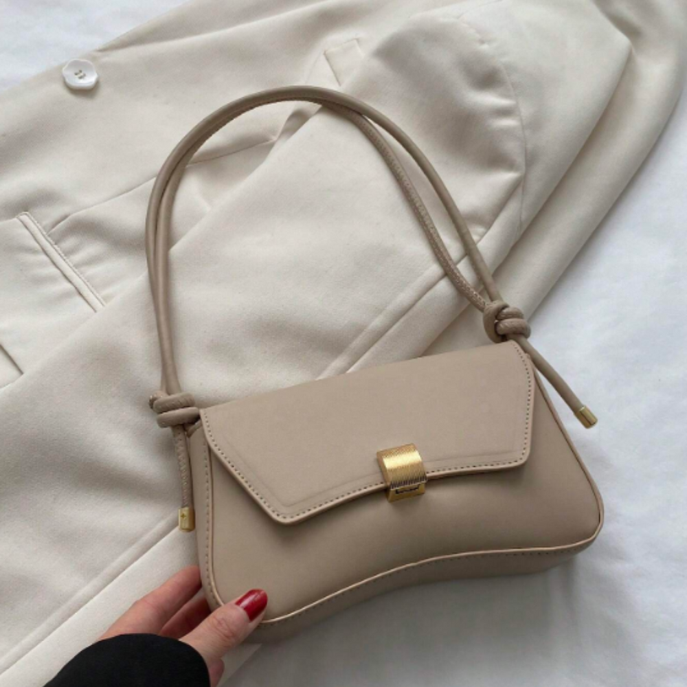 Beigefarbene Handtasche aus Leder mit goldener Schnalle auf weißem Blazer. Elegante Damenmode, stilvolles Accessoire, modische Tasche.