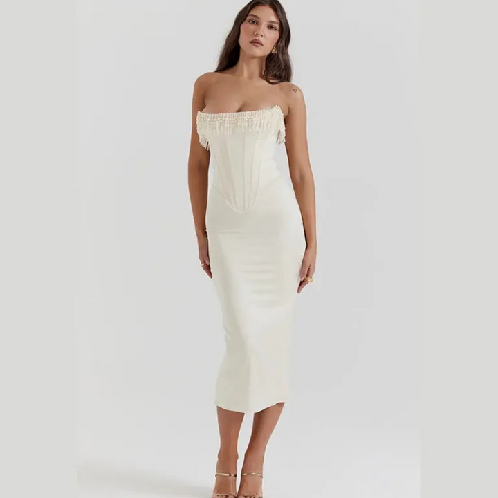 Frau in elegantem, schulterfreiem weißen Kleid mit Fransen, stehend vor neutralem Hintergrund. Mode, Abendkleid, Damenbekleidung, stilvoll.