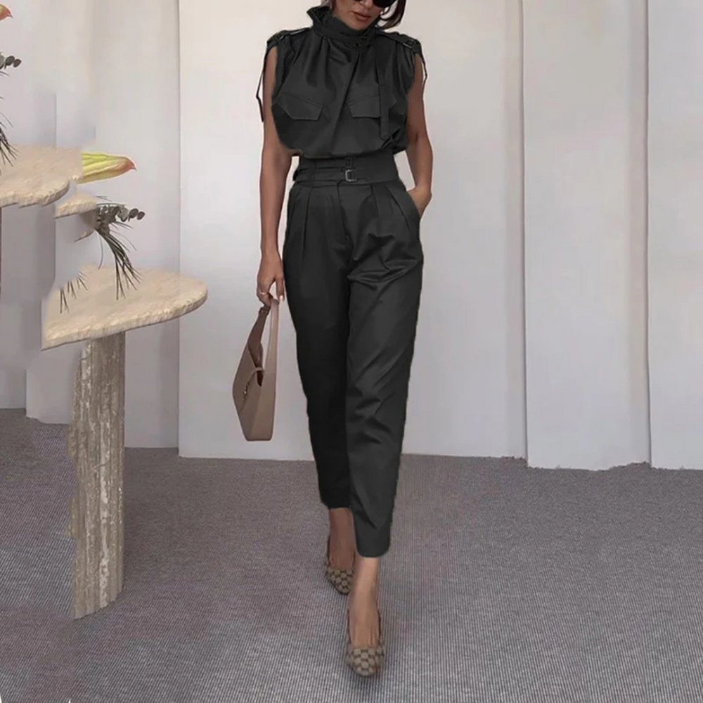 Dame in schwarzem Jumpsuit mit Gürtel, hält braune Handtasche, trägt gemusterte Pumps. Elegante Mode, stilvolles Outfit, moderne Damenbekleidung.