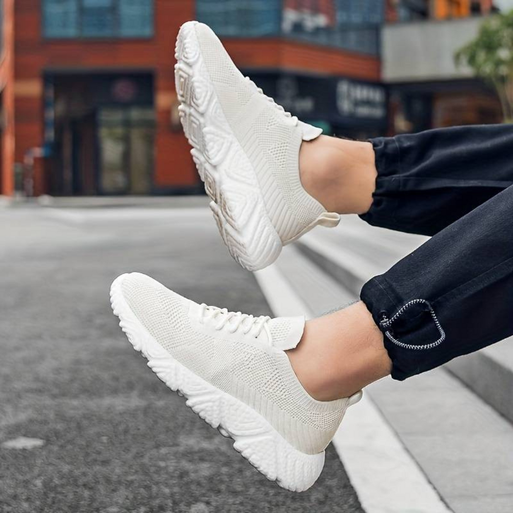 Weiße Sneaker auf grauem Asphalt, getragen von Person in schwarzer Hose. Moderne, leichte Sportschuhe, ideal für urbanen Lifestyle und Freizeit.