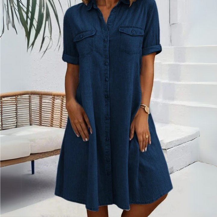 Damen Jeanskleid, knielang, mit kurzen Ärmeln und Knopfleiste, vor weißer Treppe und Rattanbank. Sommermode, Freizeitkleidung, Denim-Look.