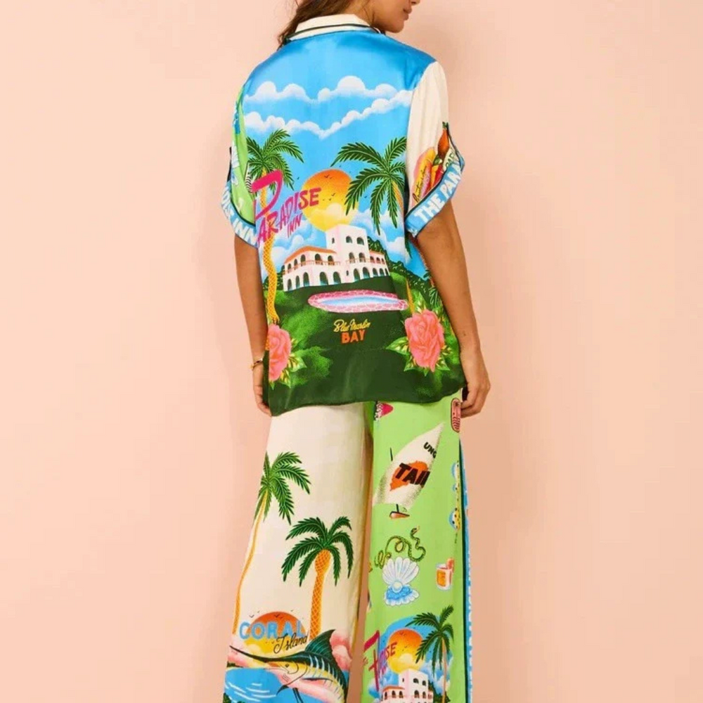 Frau in bunter, tropischer Sommerkleidung mit Palmen- und Strandmotiv, Rückansicht. Ideal für Urlaub, Strandmode, tropische Outfits.