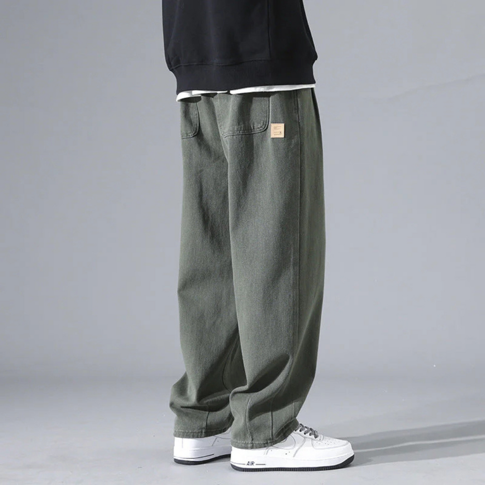 Weite grüne Baggy-Jeans für Herren, kombiniert mit weißen Sneakers und schwarzem Sweatshirt. Modetrend, lässiger Streetwear-Stil.