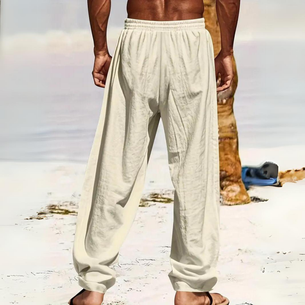 Mann in weißen Leinenhosen am Strand, barfuß im Sand. Sommermode, Strandkleidung, entspannter Look. Ideal für warme Tage und Freizeitaktivitäten.