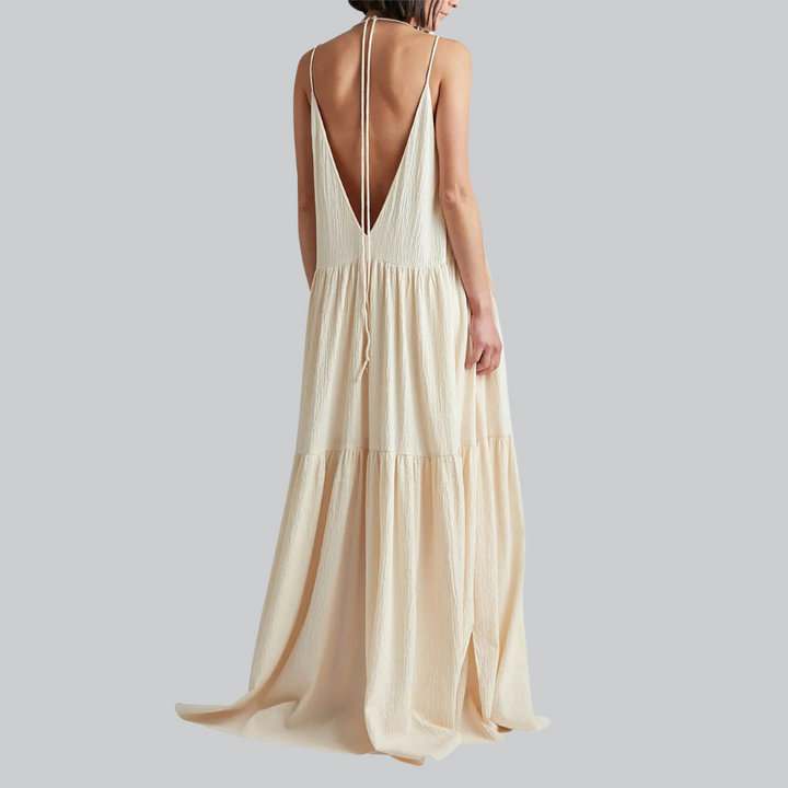 Frau in langem, cremefarbenem Sommerkleid mit tiefem Rückenausschnitt, elegantes Design, modisch, luftiger Stoff, ideal für warme Tage.