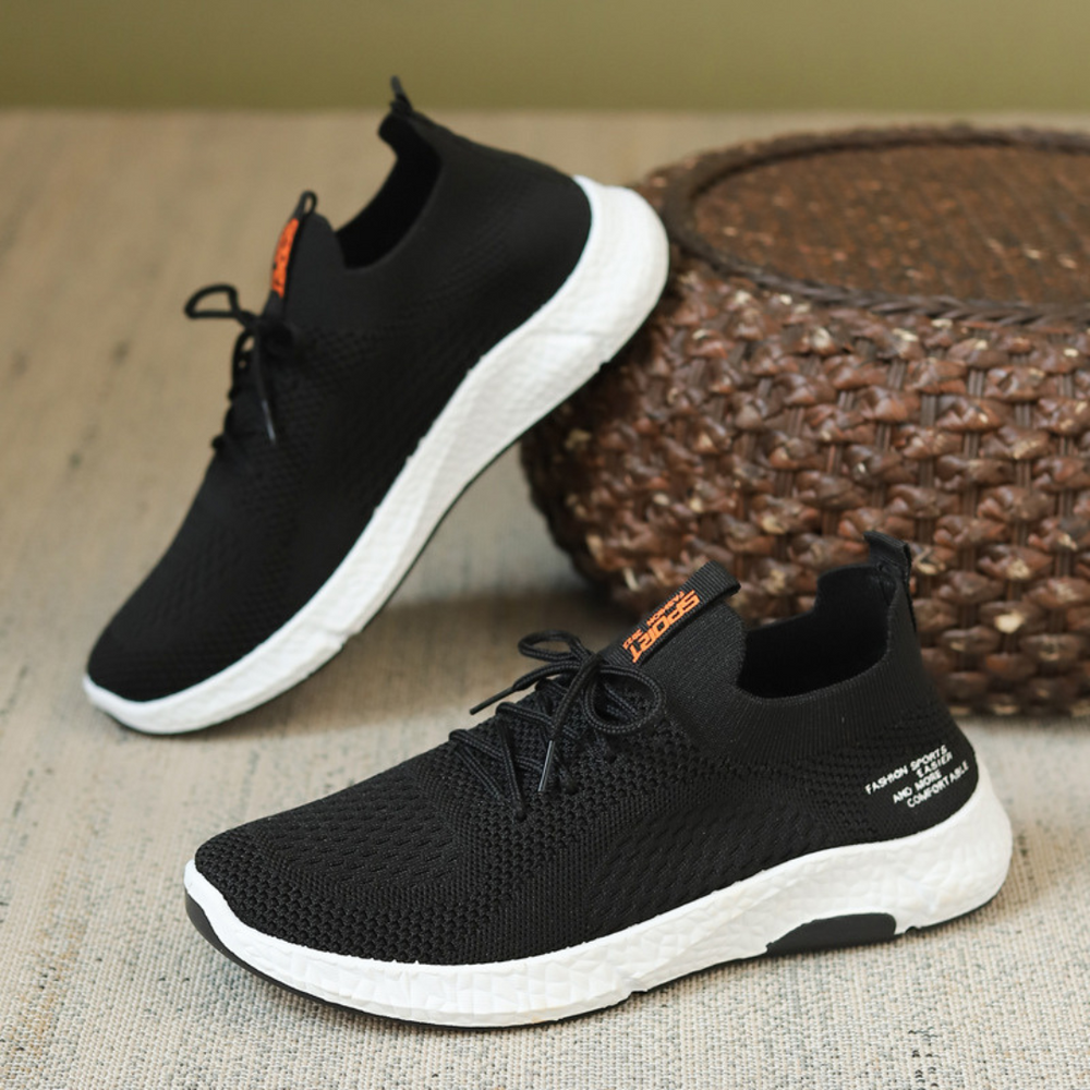 Schwarze Sneaker mit weißer Sohle auf einem Tisch, gestricktes Obermaterial, sportliches Design, ideal für Laufen und Freizeit, moderne Herrenmode.