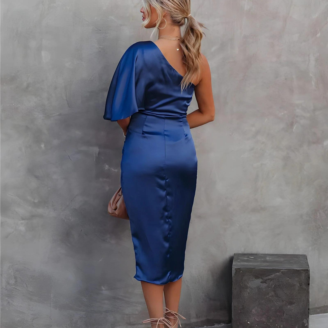 Frau in elegantem, blauem Satinkleid mit asymmetrischem Schnitt, steht vor grauer Wand. Abendmode, schulterfreies Design, stilvolle Kleidung.