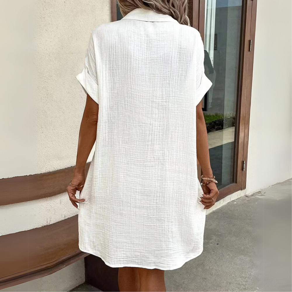 Frau in weißem Leinenkleid, Rückansicht, vor modernem Gebäude. Sommermode, lässiger Stil, elegantes Design, ideal für warme Tage.