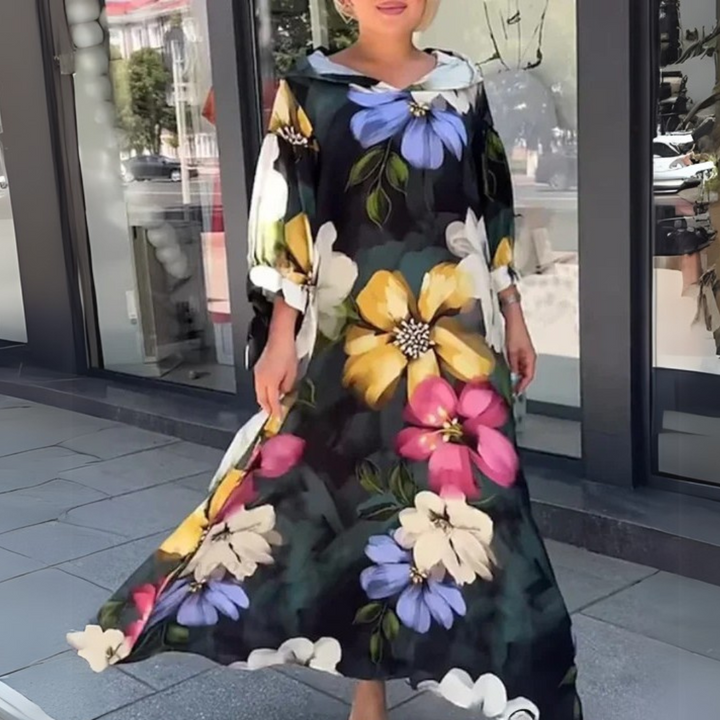 Frau in einem eleganten, geblümten Maxikleid vor einem Schaufenster. Sommermode, florales Design, stilvolle Damenbekleidung, Stadtbummel.