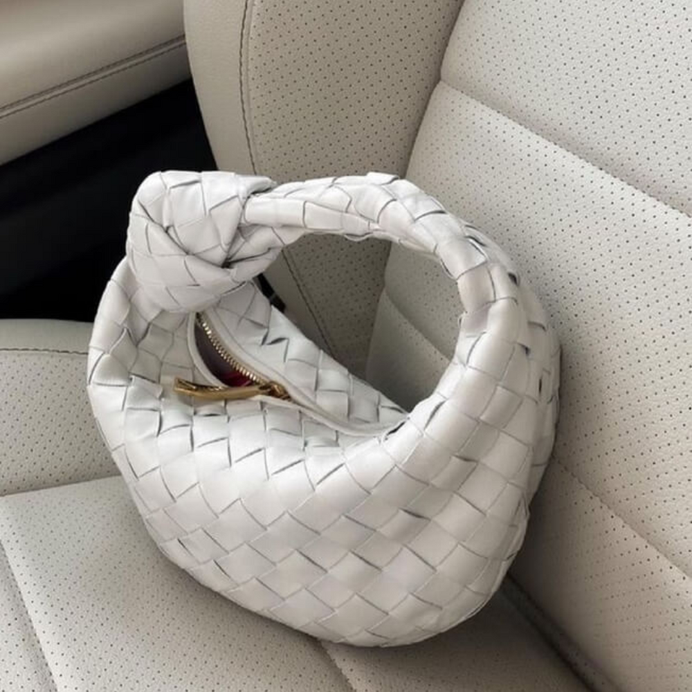 Weiße, geflochtene Handtasche auf beigem Autositz. Luxuriöses Design, modisches Accessoire, hochwertige Materialien, stilvoll und elegant.