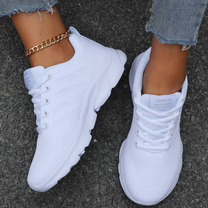 Weiße Sneaker auf Asphalt, getragen mit zerrissenen Jeans und goldener Knöchelkette. Modische Damen-Sportschuhe, ideal für Freizeit und Streetstyle.