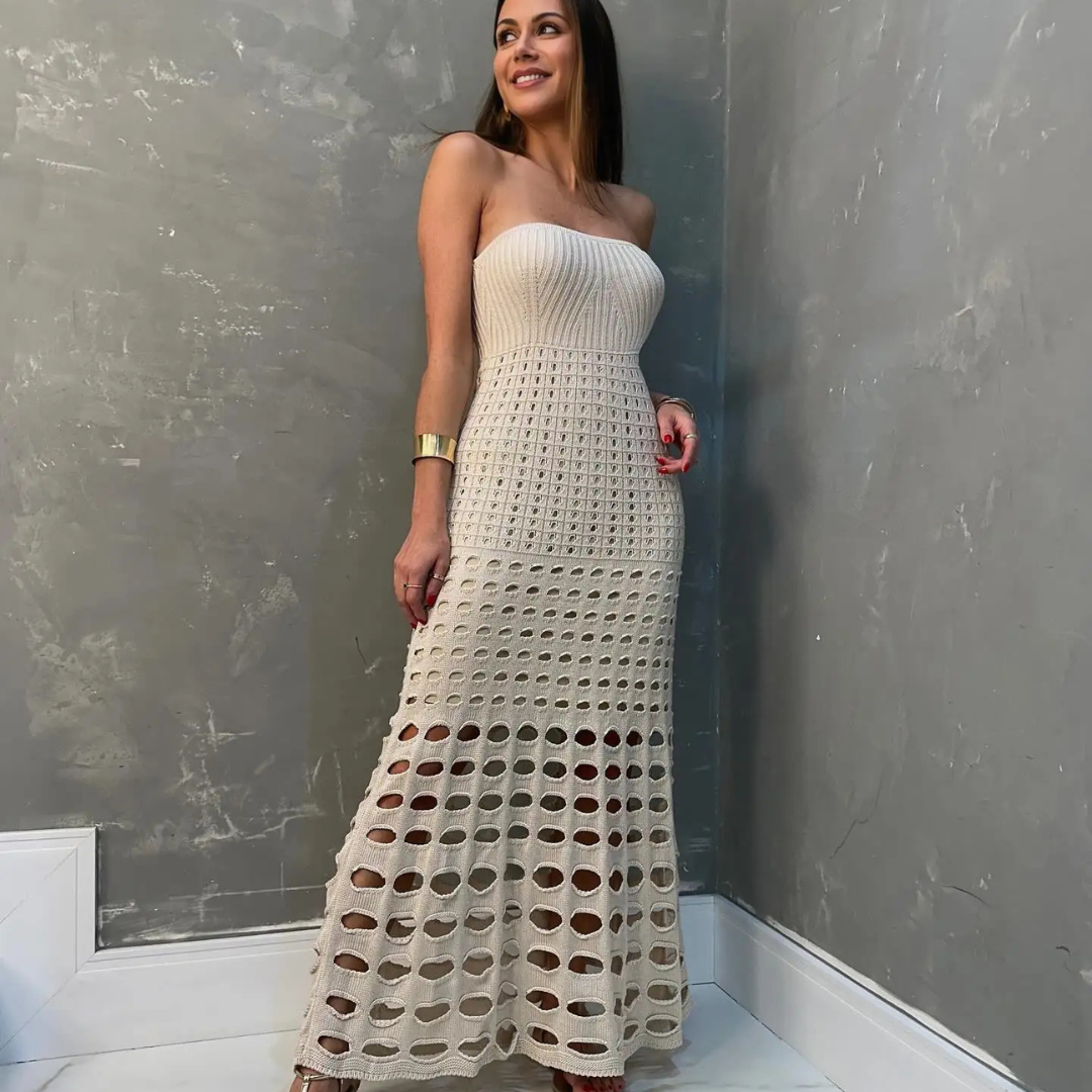 Frau in elegantem, cremefarbenem Häkelkleid vor grauer Wand. Modetrend, Sommerkleid, stilvolle Damenmode, schulterfreies Design.