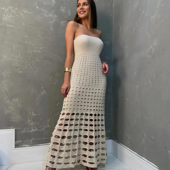Frau in elegantem, cremefarbenem Häkelkleid vor grauer Wand. Modetrend, Sommerkleid, stilvolle Damenmode, schulterfreies Design.
