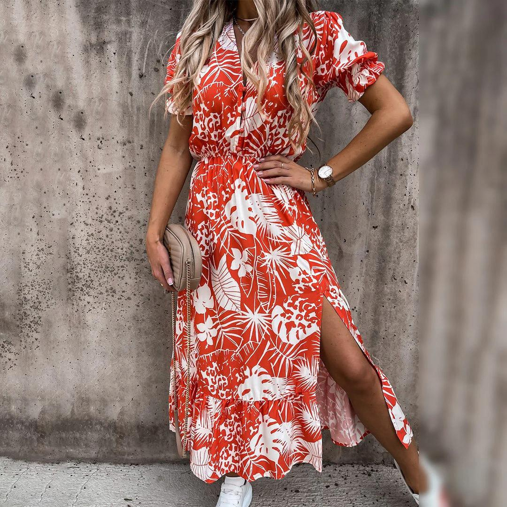 Frau in rotem, geblümtem Sommerkleid mit seitlichem Schlitz, trägt weiße Sneaker und beige Handtasche, vor grauer Betonwand. Fashion, Sommermode.