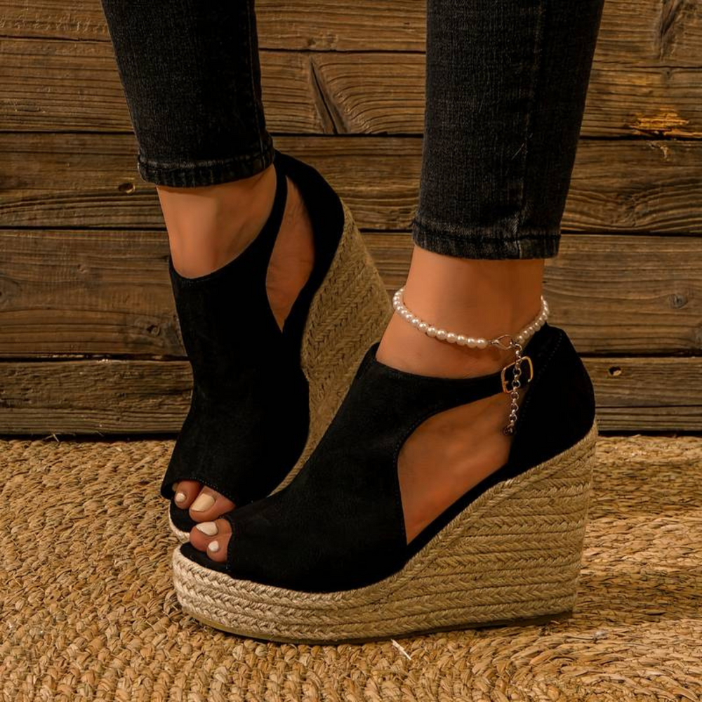 Schwarze Keilsandaletten mit offener Spitze und Bastsohle, getragen mit schwarzer Jeans. Elegante Damenmode, ideal für Sommer und Freizeit.