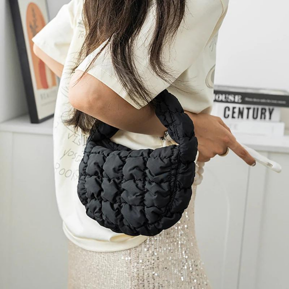 Frau mit schwarzer, gesteppter Handtasche, modisch, elegant, in modernem Raum. Perfekt für trendige Outfits und stilvolle Accessoires.