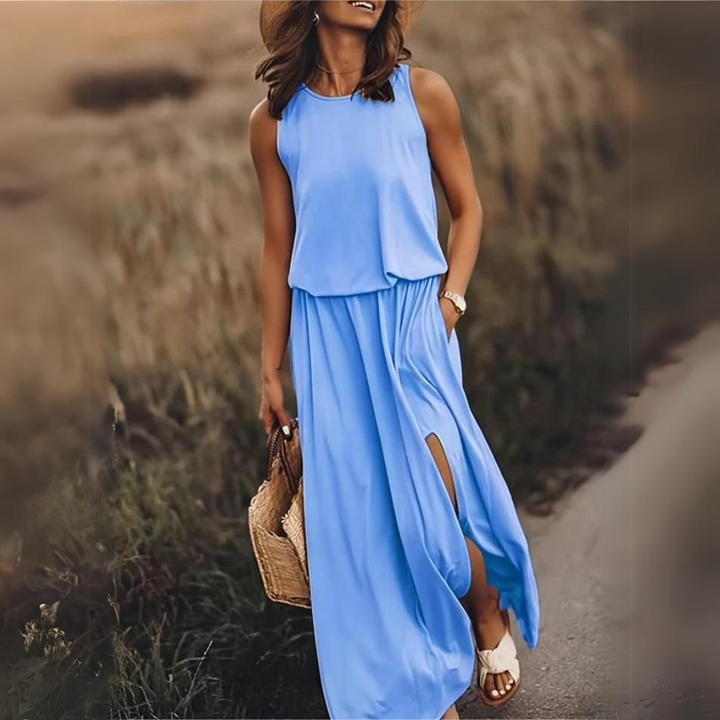 Frau in blauem Sommerkleid mit Schlitz, Strohhut und Sandalen spaziert auf einem ländlichen Weg. Perfektes Outfit für Sommermode und Freizeit.