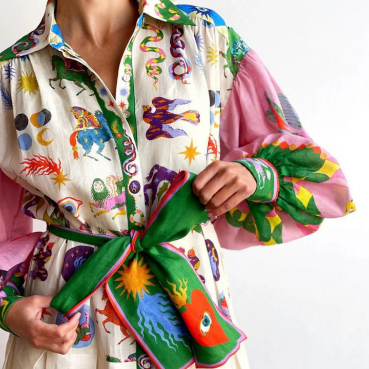 Bunte Bluse mit astrologischen Motiven und auffälligen Mustern, kombiniert mit grünem Gürtel. Modetrend, auffällige Kleidung, Astrologie-Design.