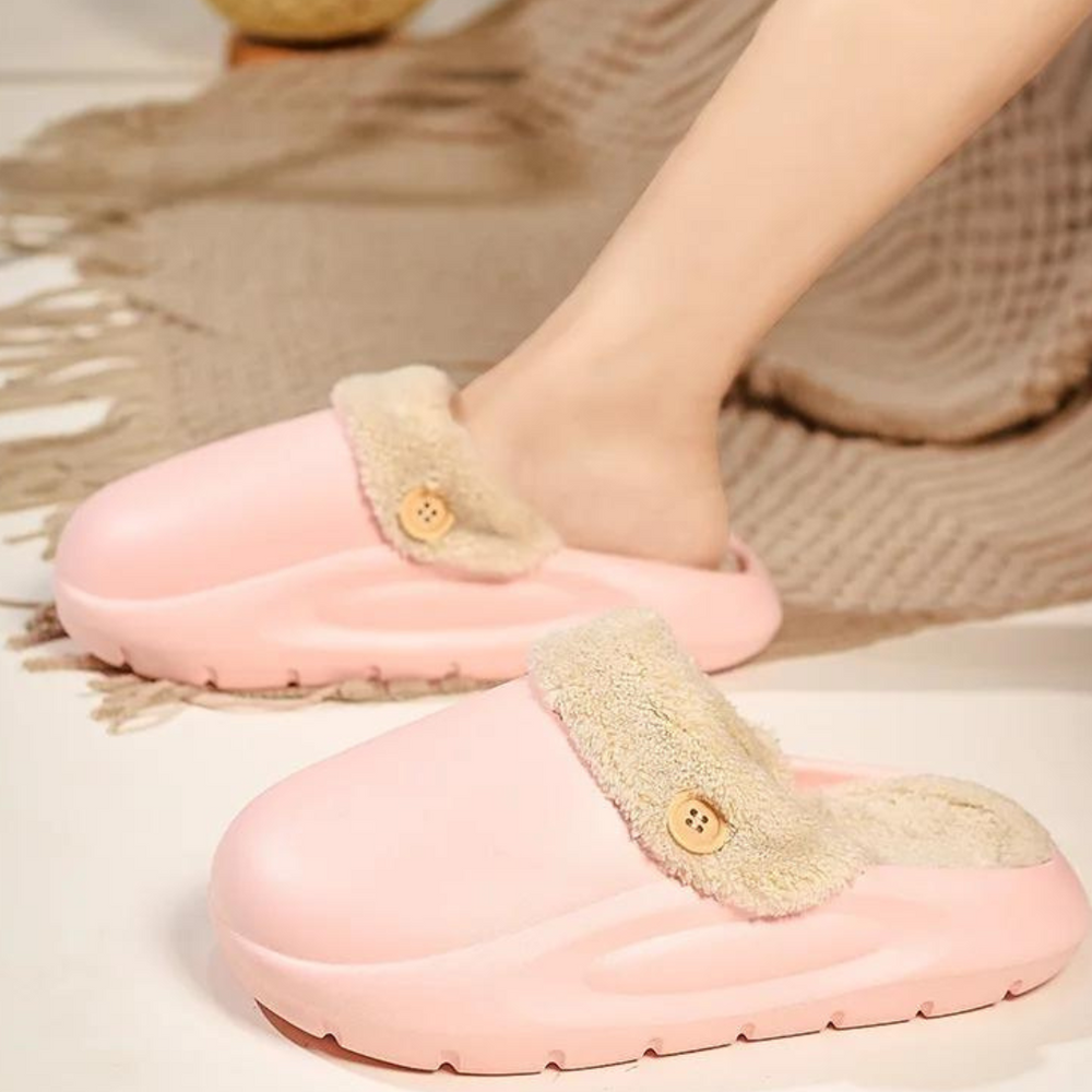 Rosa Hausschuhe mit Plüschfutter und Knopfdetail auf Teppich. Bequeme, warme Pantoffeln für Damen, ideal für den Winter.