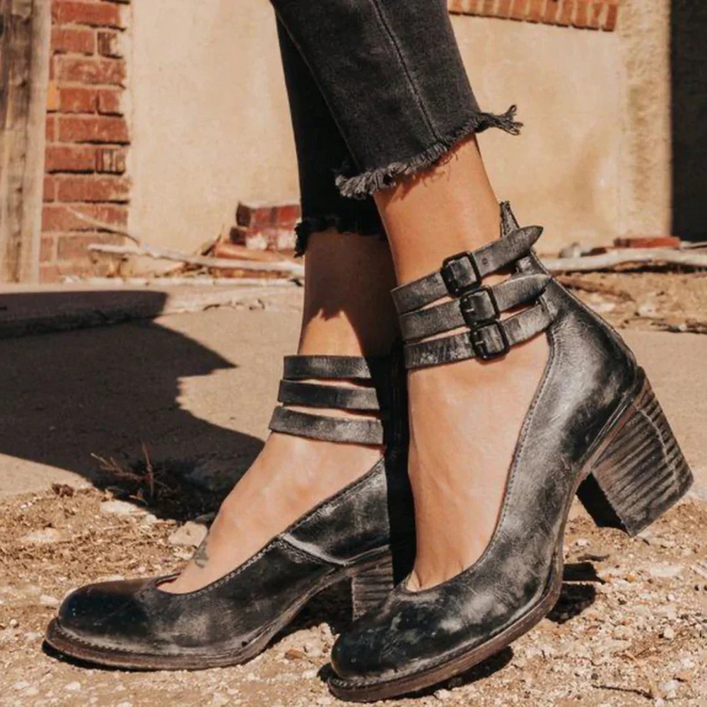 Schwarze Vintage-Lederstiefeletten mit Blockabsatz und Schnallen, getragen von einer Person in schwarzer Jeans. Modische Damenstiefel im Retro-Stil.