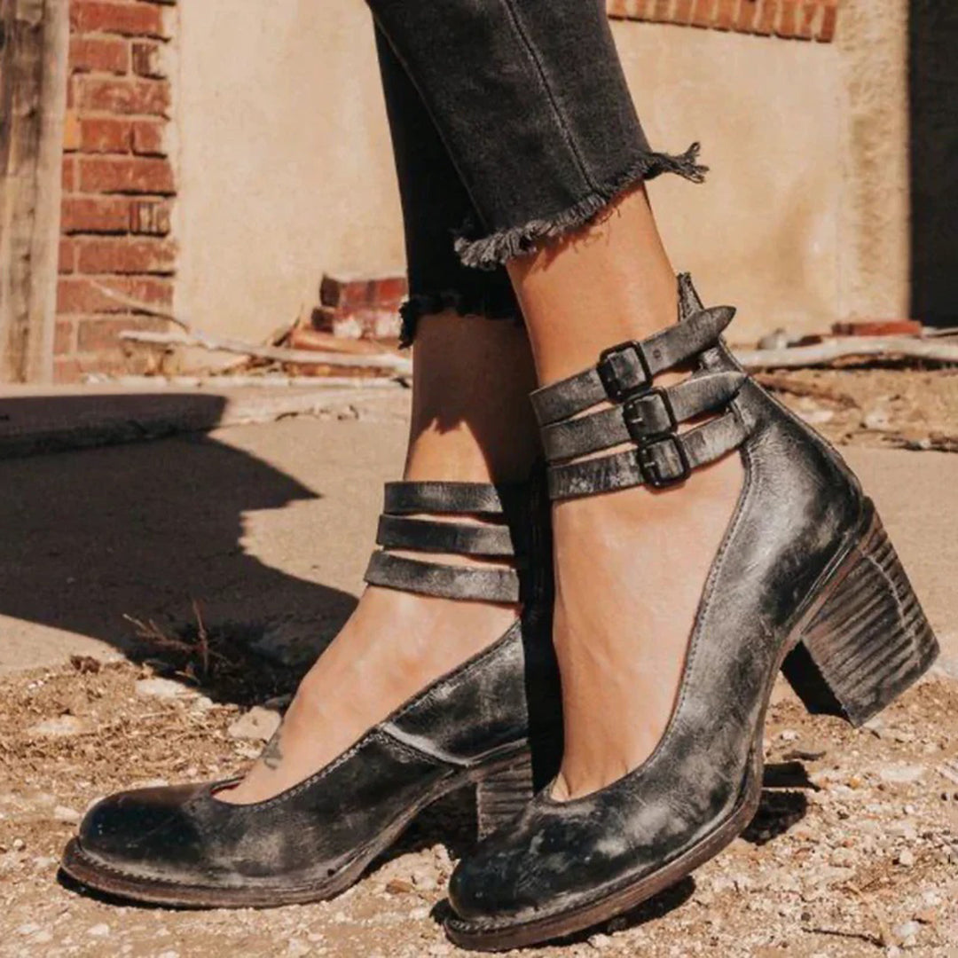 Schwarze Vintage-Lederstiefeletten mit Blockabsatz und Schnallen, getragen von einer Person in schwarzer Jeans. Modische Damenstiefel im Retro-Stil.