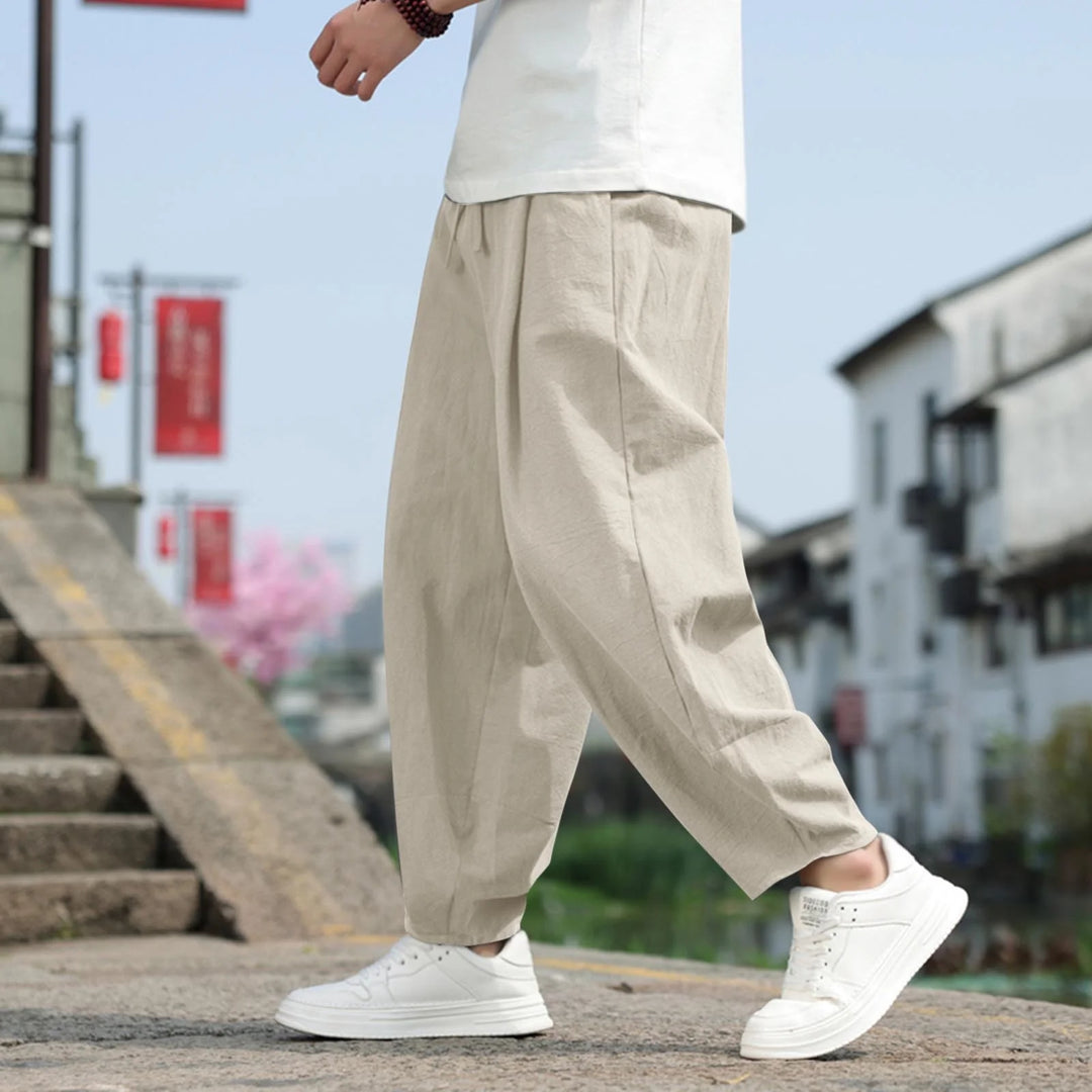 Person in beiger Leinenhose und weißen Sneakers geht eine Steintreppe hinauf. Hintergrund zeigt traditionelle Architektur und rote Banner.