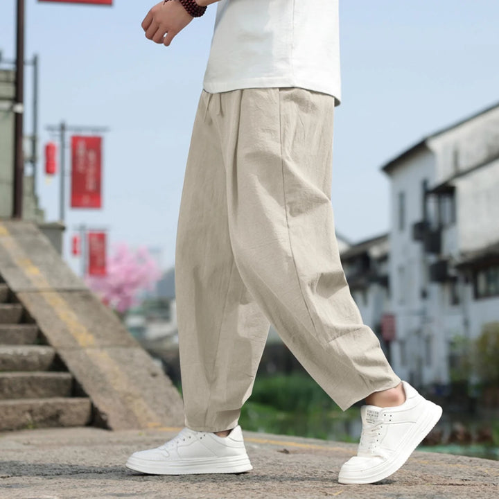 Person in beiger Leinenhose und weißen Sneakers geht eine Steintreppe hinauf. Hintergrund zeigt traditionelle Architektur und rote Banner.