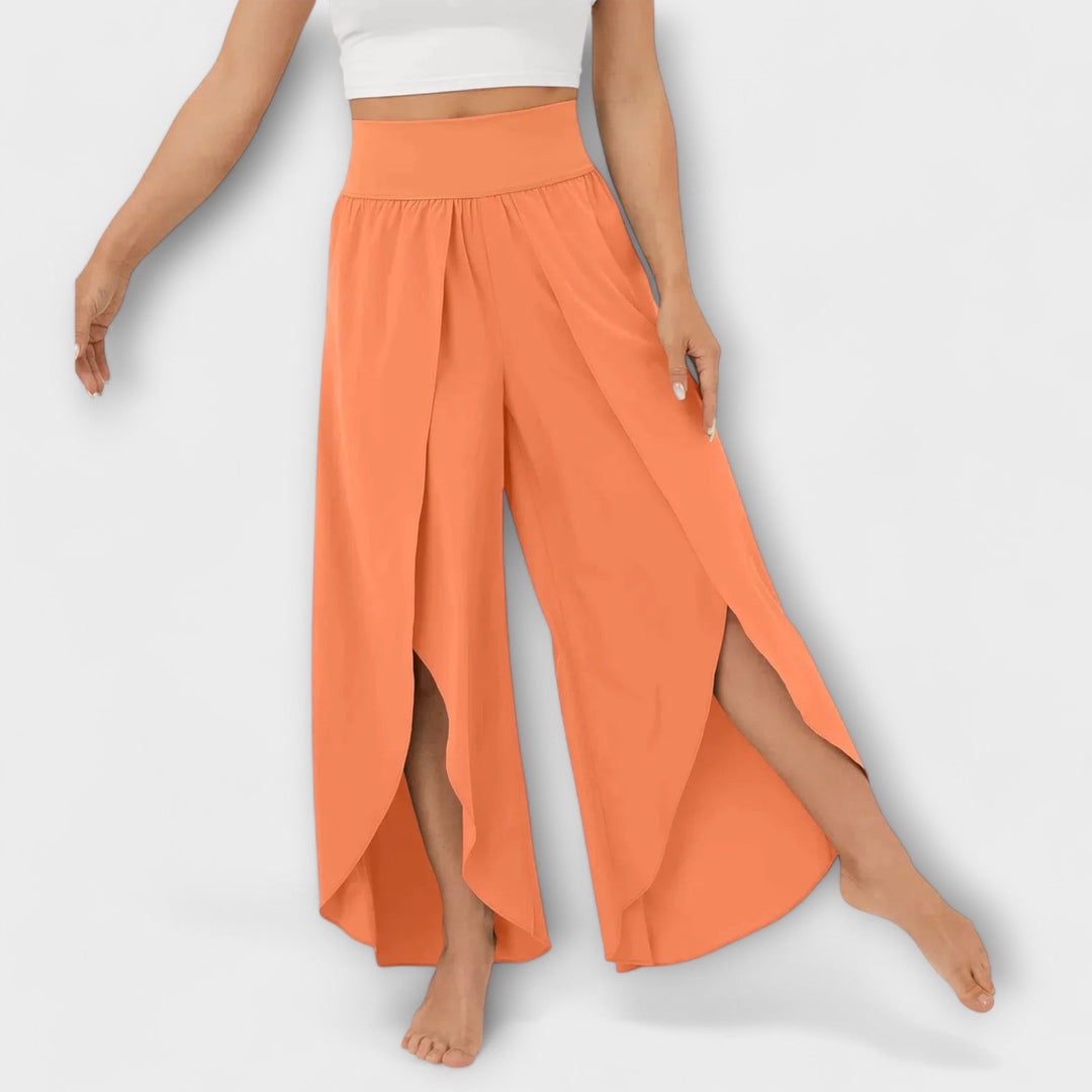 Frau in orangefarbenen, weiten Hosen mit seitlichen Schlitzen, barfuß, vor weißem Hintergrund. Modetrend, Damenbekleidung, Sommeroutfit.