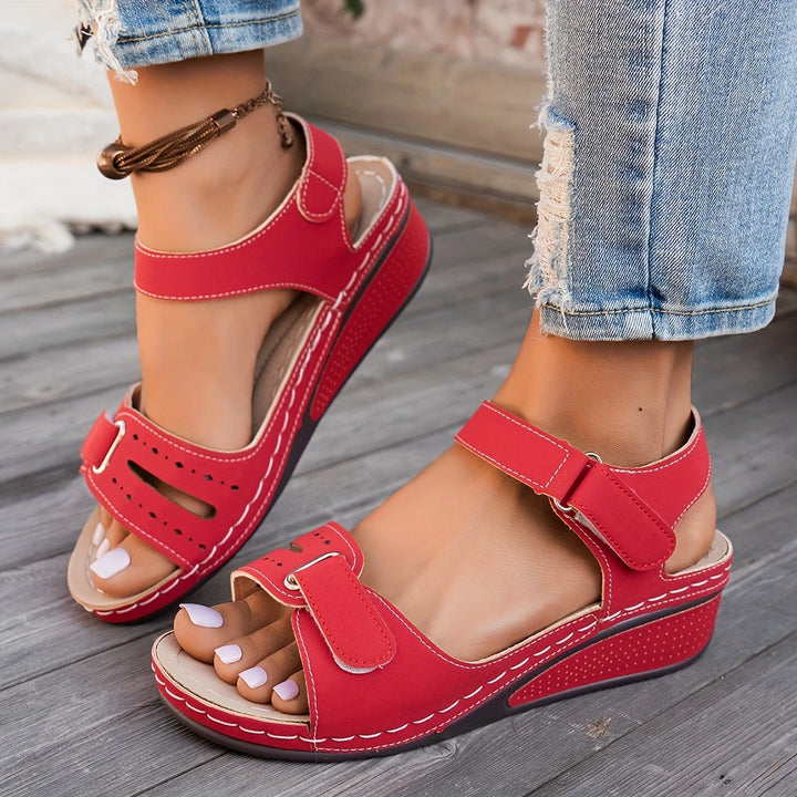Rote Damen-Sandalen mit Klettverschluss und Keilabsatz, getragen mit zerrissenen Jeans. Bequeme Sommerschuhe für Damenmode.