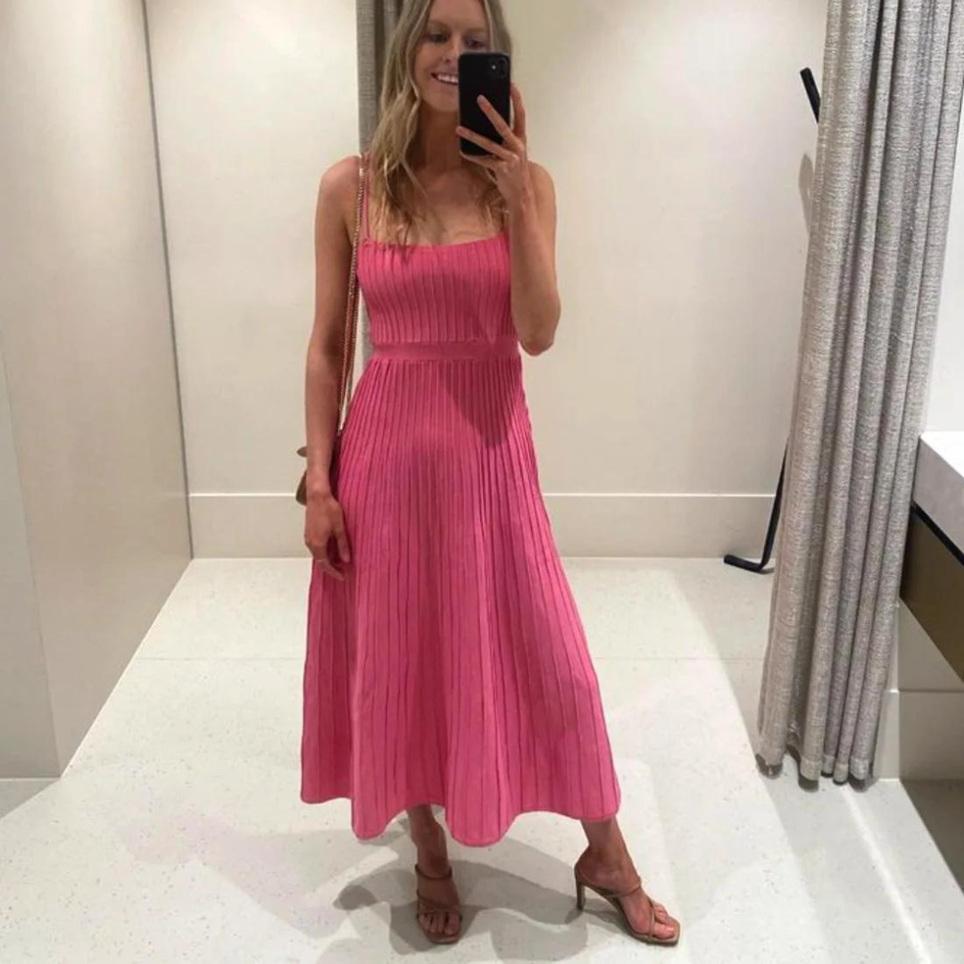 Frau in rosa, plissiertem Kleid macht Selfie im Spiegel. Elegantes Sommeroutfit, modische Sandalen, Umkleidekabine, stilvoller Look.