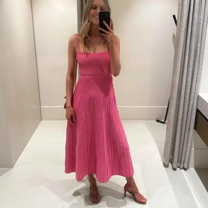 Frau in rosa, plissiertem Kleid macht Selfie im Spiegel. Elegantes Sommeroutfit, modische Sandalen, Umkleidekabine, stilvoller Look.