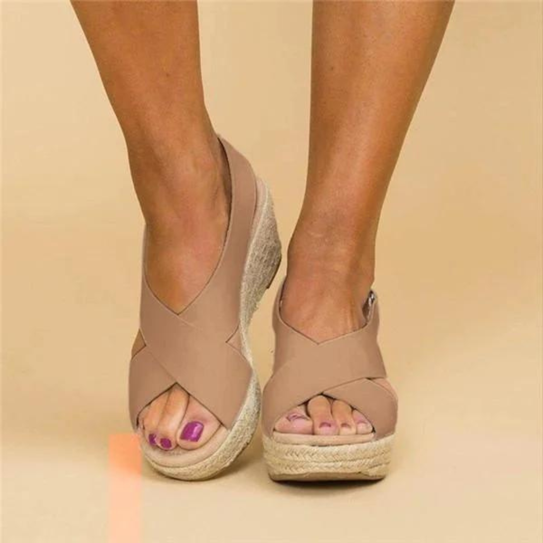 Beige Damen-Wedges mit Kreuzriemen und Espadrille-Sohle, getragen an gebräunten Beinen. Modische Sommerschuhe für Damen.