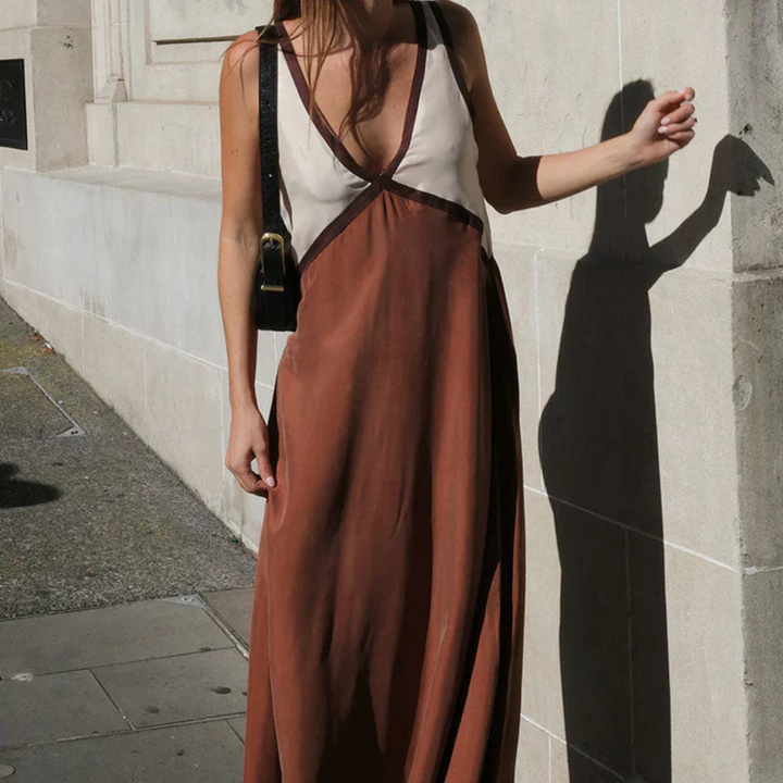 Braunes Maxikleid mit tiefem V-Ausschnitt, getragen von einer Frau auf einer städtischen Straße. Sommermode, elegantes Design, lässiger Stil.