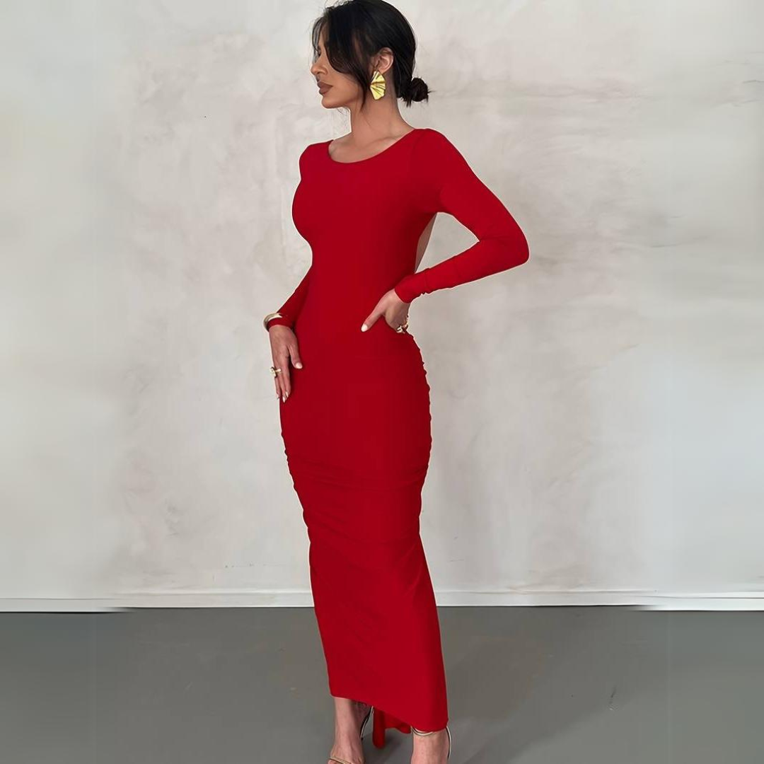 Frau in elegantem, figurbetontem roten Kleid, seitlich stehend, mit hochgestecktem Haar und goldenen Ohrringen, vor neutralem Hintergrund.
