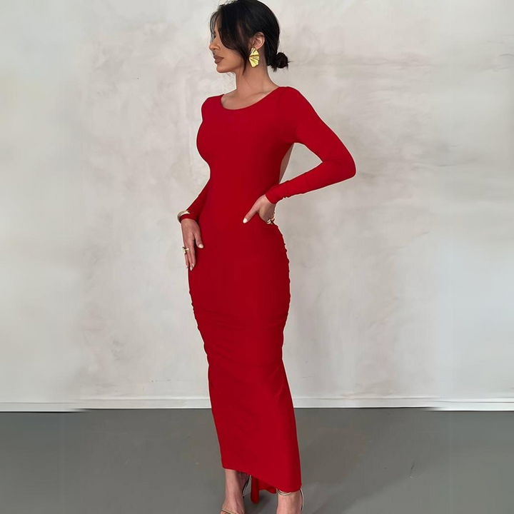 Frau in elegantem, figurbetontem roten Kleid, seitlich stehend, mit hochgestecktem Haar und goldenen Ohrringen, vor neutralem Hintergrund.