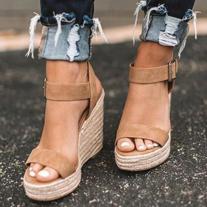 Beige Keilsandalen mit Bastsohle, getragen von einer Person mit zerrissenen Jeans auf Asphalt. Modische Sommerschuhe, Damenmode, Streetstyle.