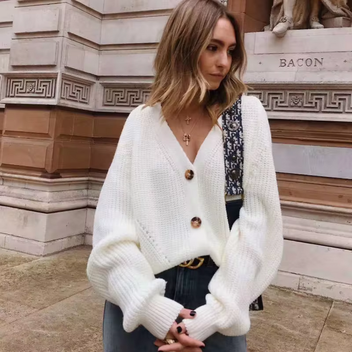 Frau in weißem Strickpullover mit Knöpfen, lässig vor historischer Architektur stehend. Modetrend, Herbstmode, Streetstyle.
