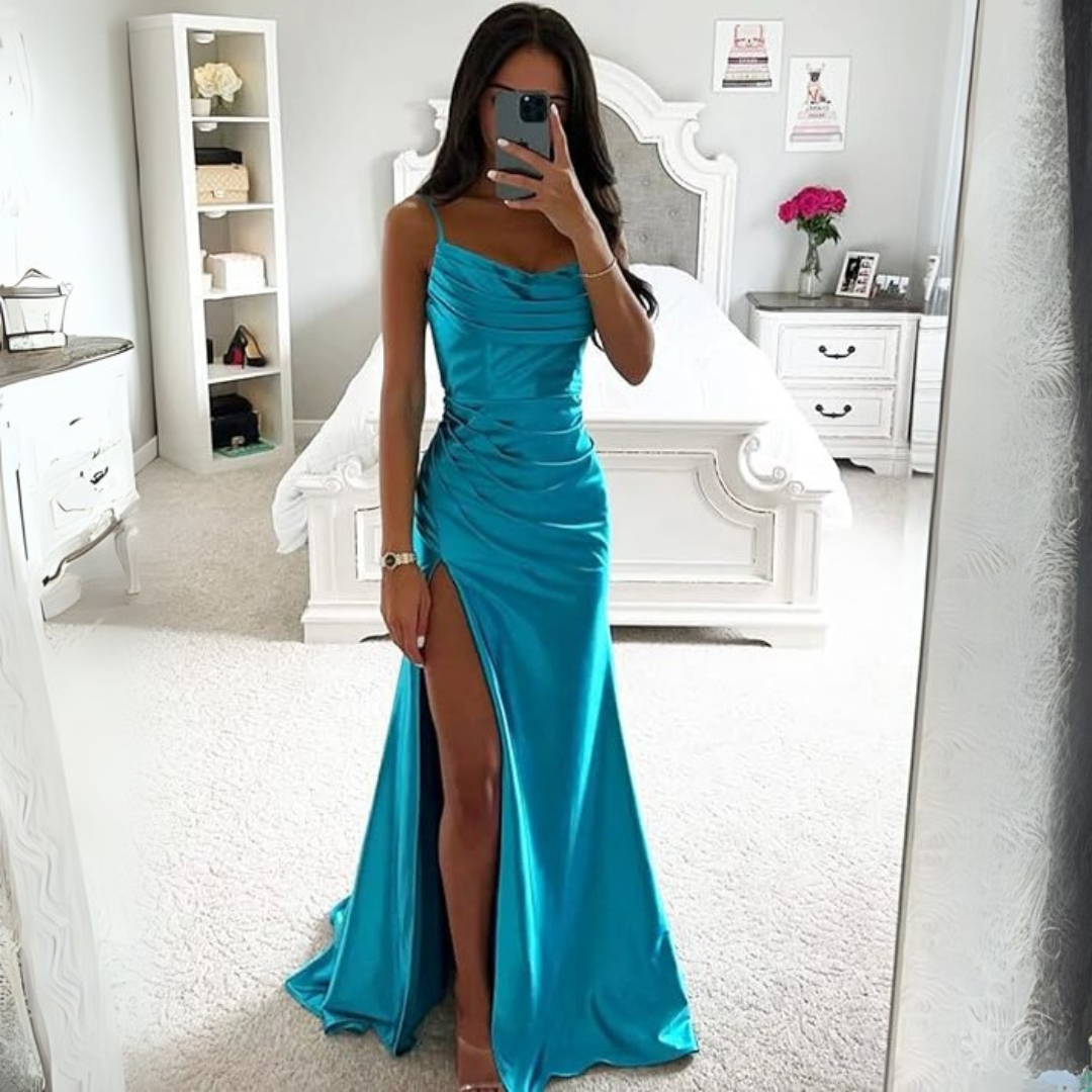 Frau in türkisfarbenem Abendkleid mit hohem Beinschlitz, steht in elegantem Schlafzimmer, macht Selfie vor weißem Bett. Elegante Mode, Abendgarderobe.