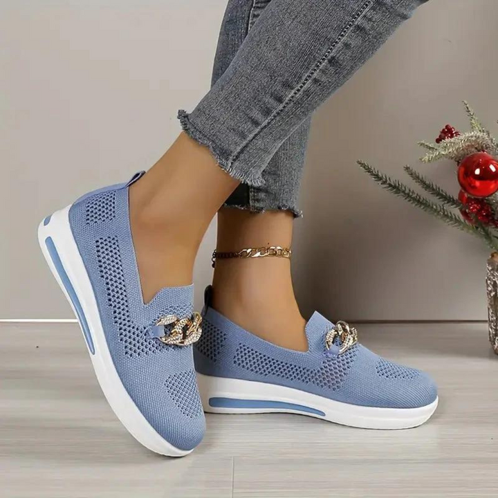 Blaue Damen-Sneaker mit Keilabsatz, Strickmuster und goldener Kette, kombiniert mit grauen Jeans. Moderne, bequeme Freizeitschuhe.
