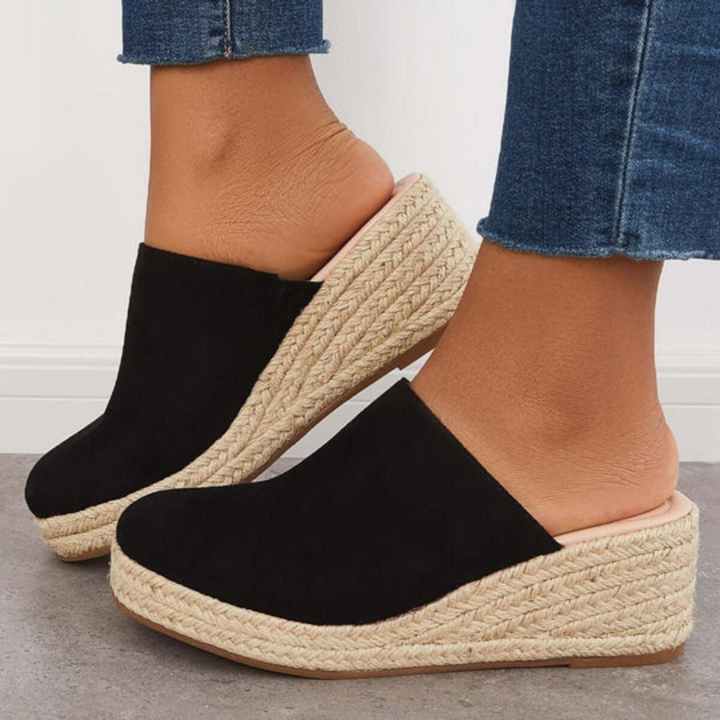 Schwarze Damen-Pantoletten mit Keilabsatz aus Bast, getragen mit blauen Jeans. Modische Sommerschuhe, bequem und stilvoll für den Alltag.